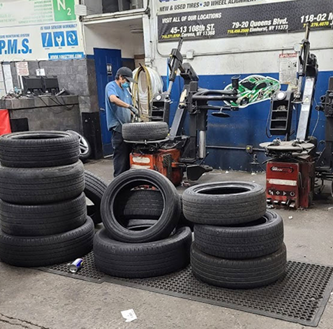 Tire shop with stacks of tires, a mechanic working, and mounted wheels on machines. | 106 St Tire and Wheel