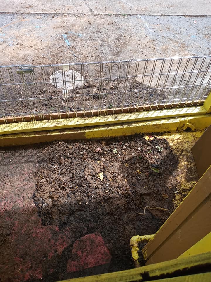 A dirty window with a yellow frame and a fence in the background.