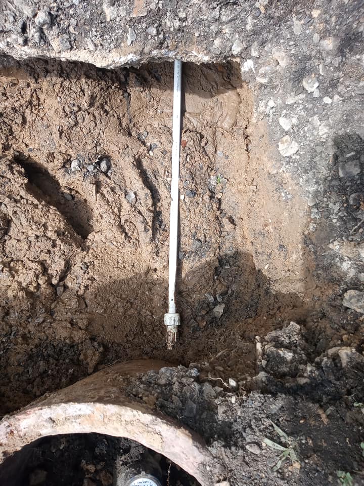 A metal pipe is sticking out of the ground next to a drain.