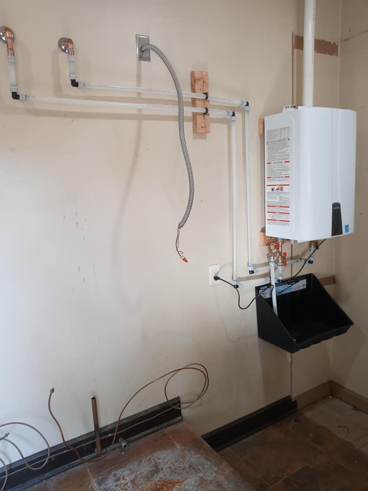 A white water heater is hanging on a wall in a room.