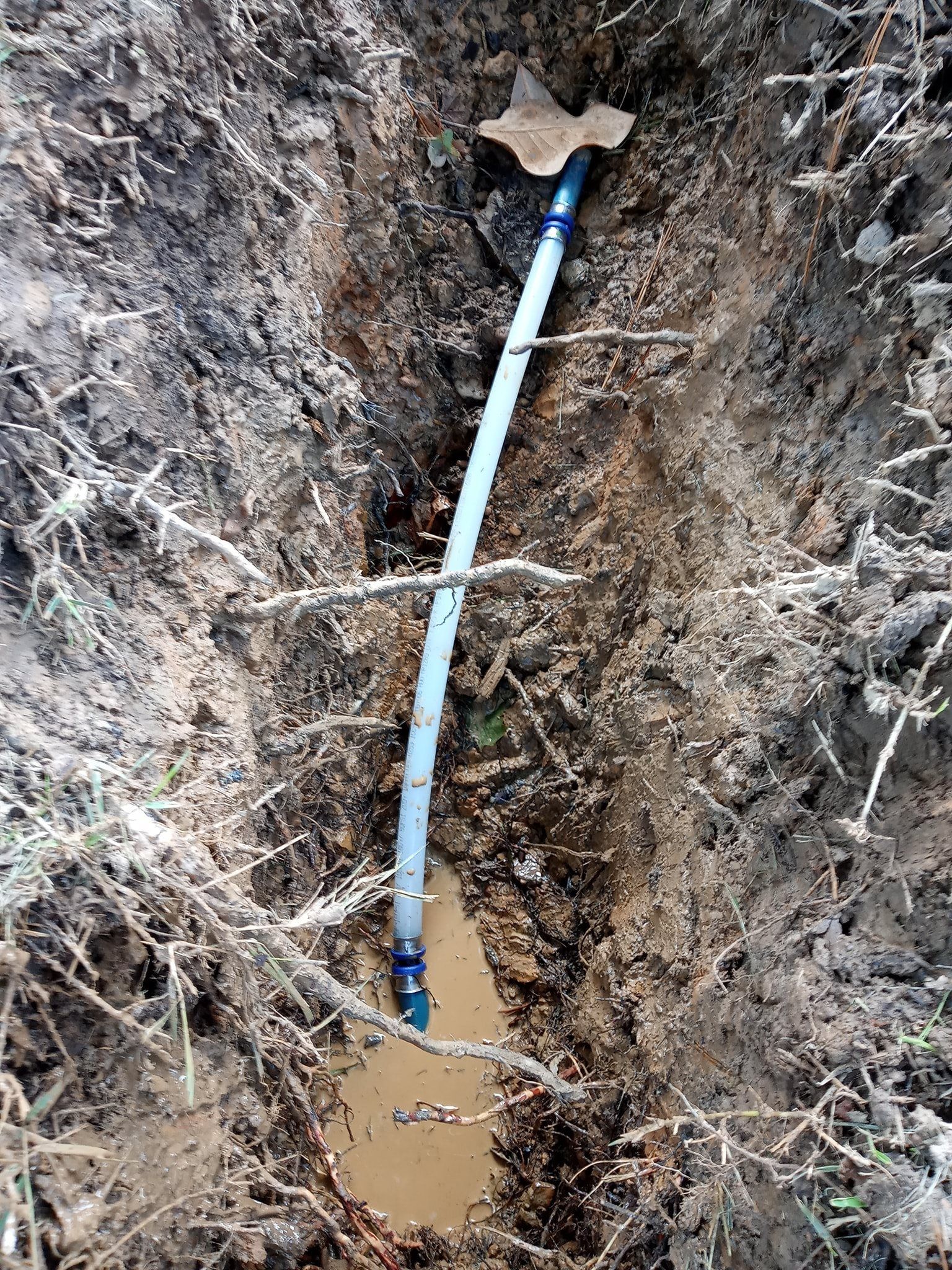 A blue pipe is laying in the dirt in a hole.