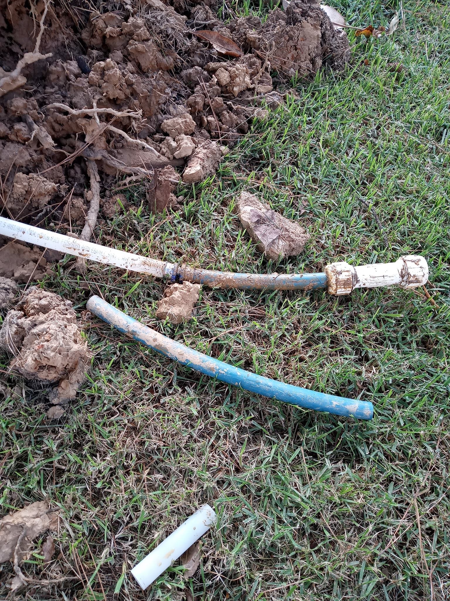 A broken hose is laying on the grass next to a pile of dirt.