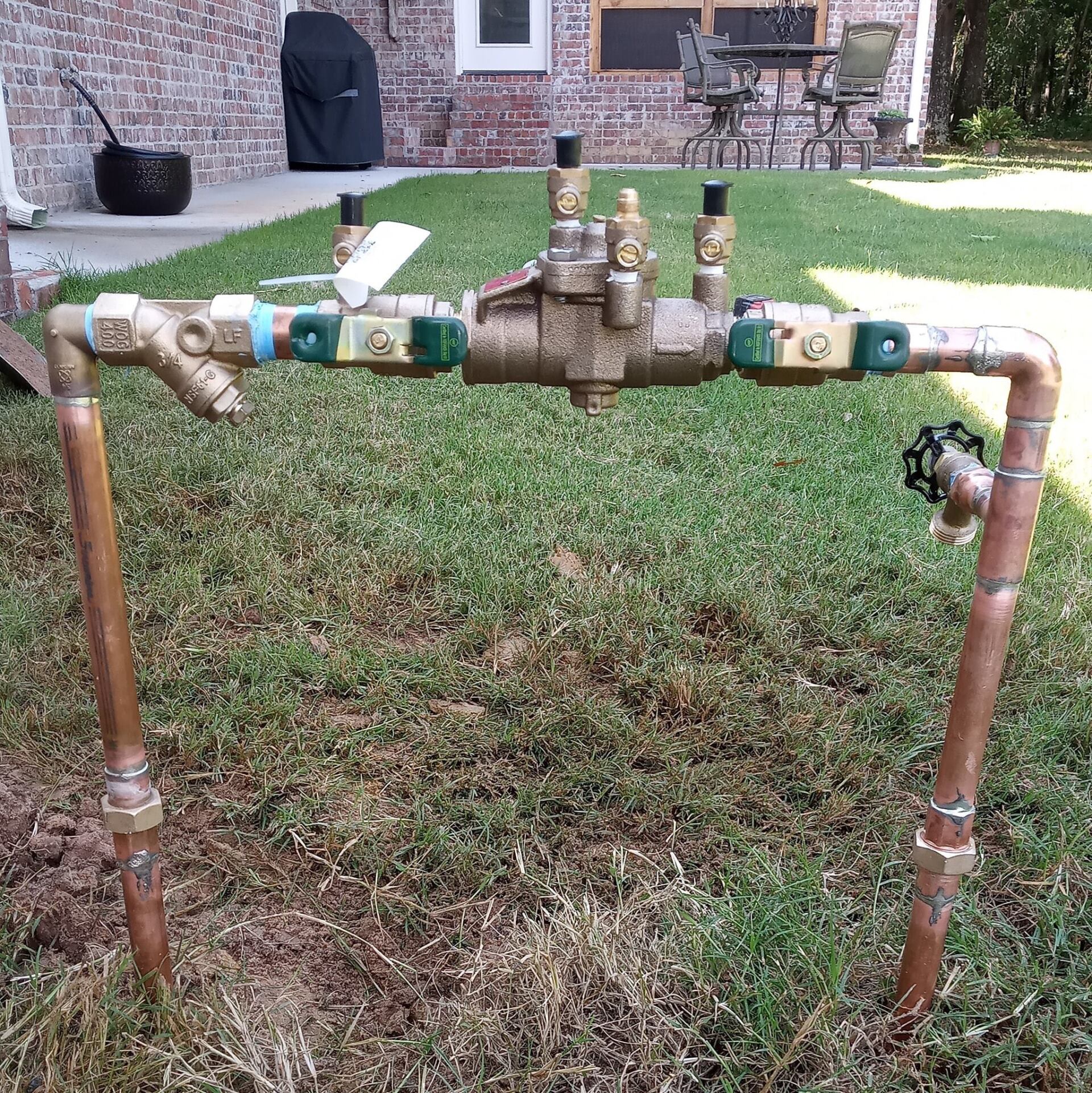 A copper pipe is sitting in the grass in front of a house.