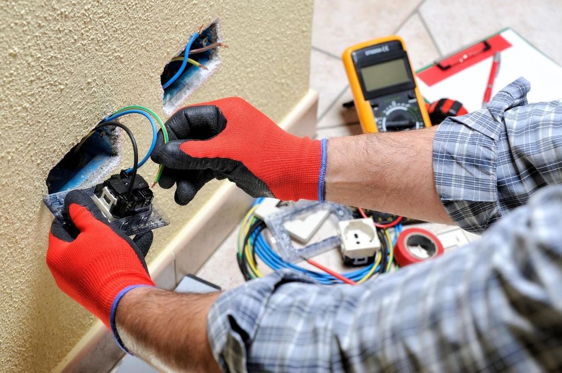 A man wearing red gloves is working on an electrical outlet.