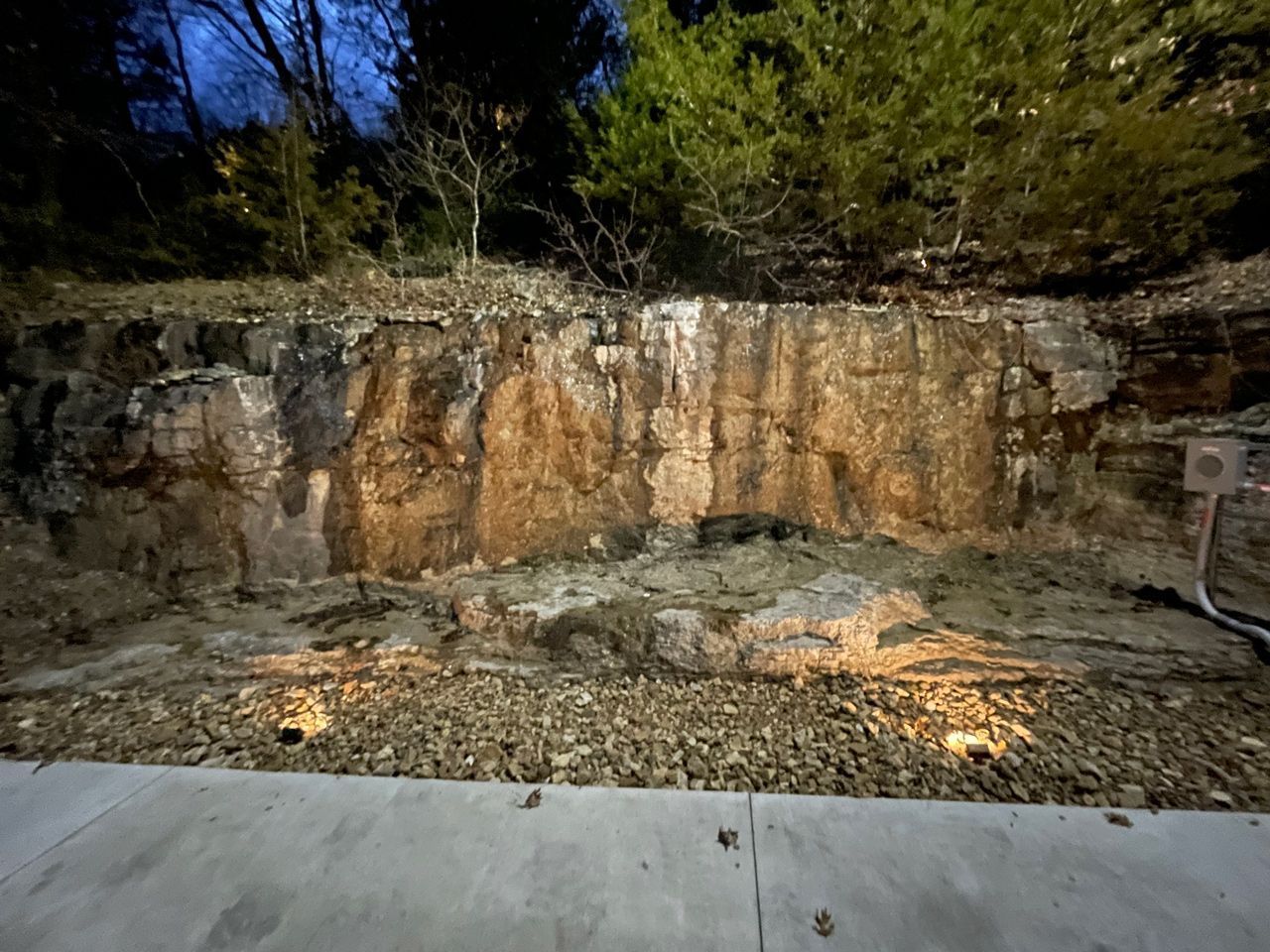 A large rock wall is lit up at night with trees in the background.