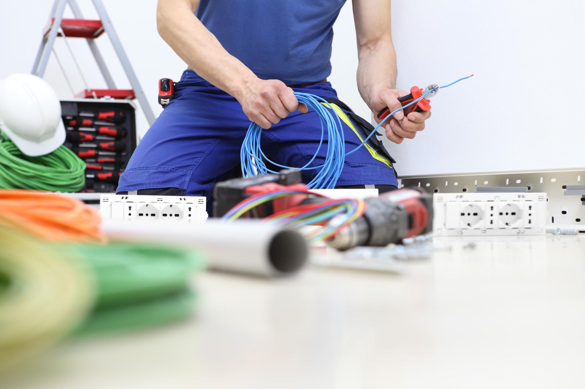 A man is kneeling on the floor holding a wire and a screwdriver.