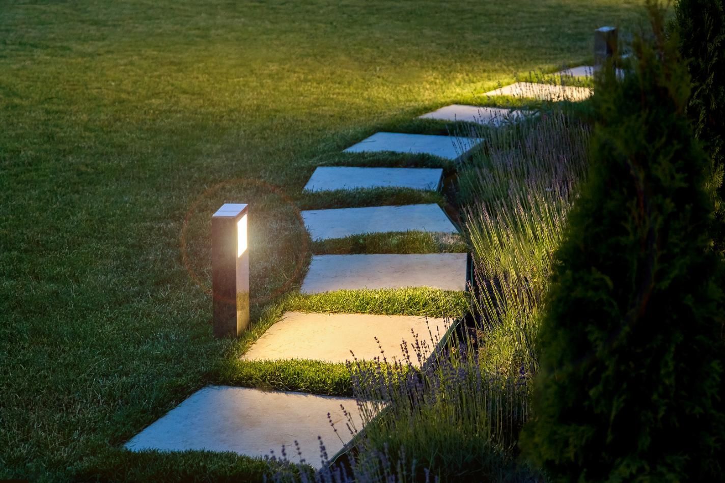 A stone walkway in a garden with a light on the side of it.