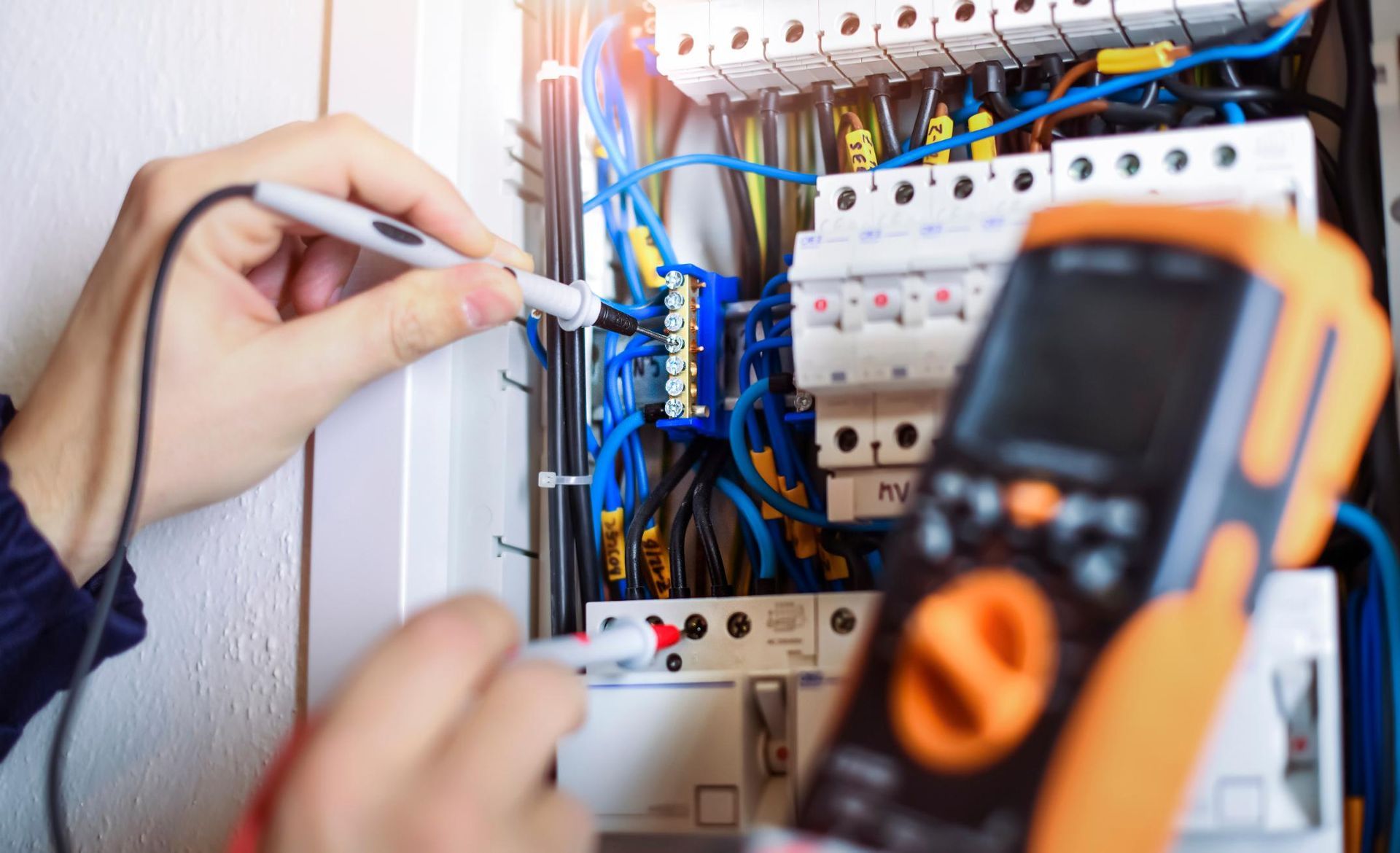 An electrician is working on an electrical box with a multimeter.