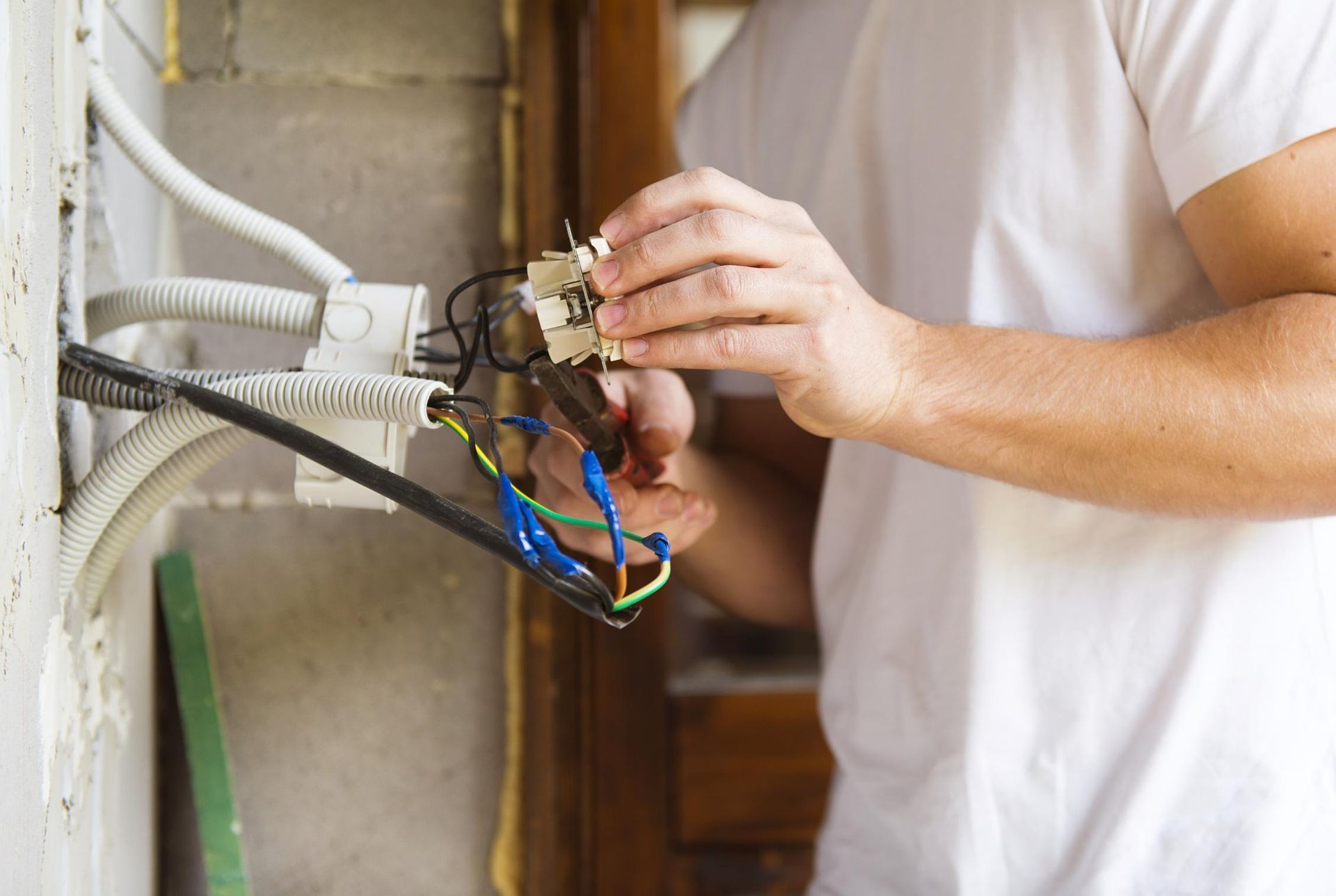 A man is fixing an electrical outlet with a pair of pliers.