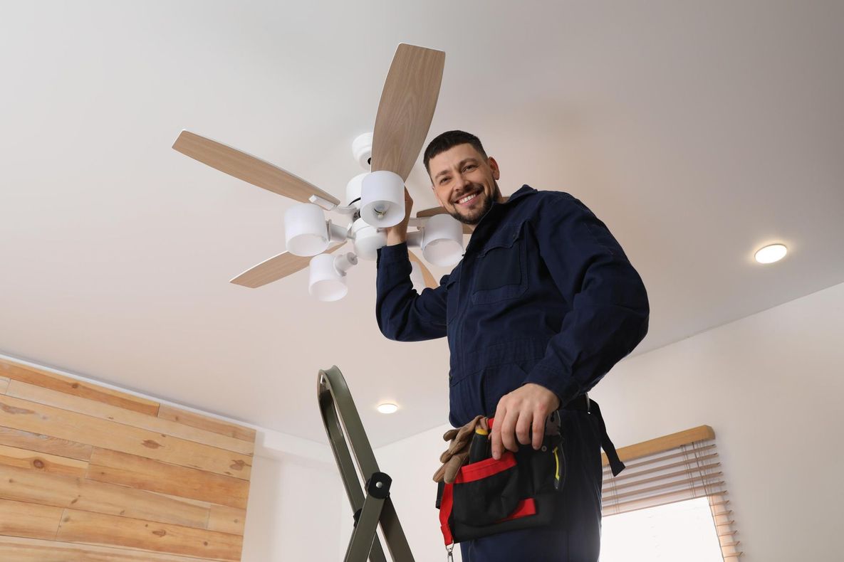 A man is standing on a ladder fixing a ceiling fan.