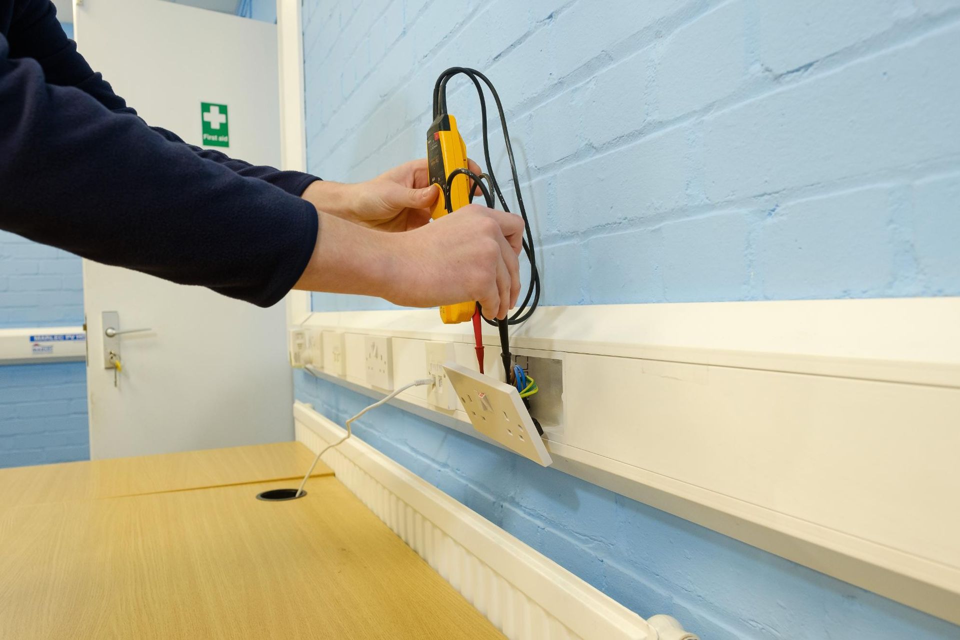 A person is working on an electrical outlet with a voltmeter.