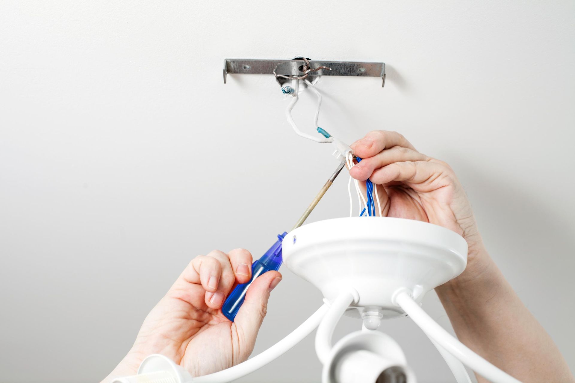 A person is fixing a chandelier with a screwdriver.