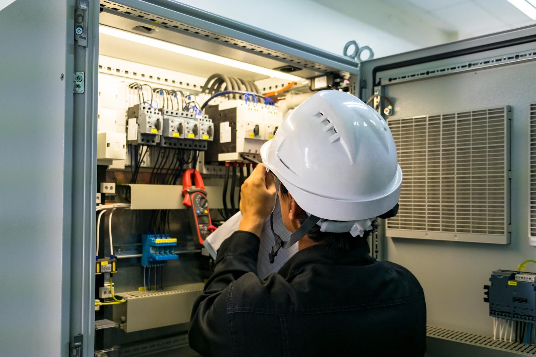 A man wearing a hard hat is working on an electrical box.