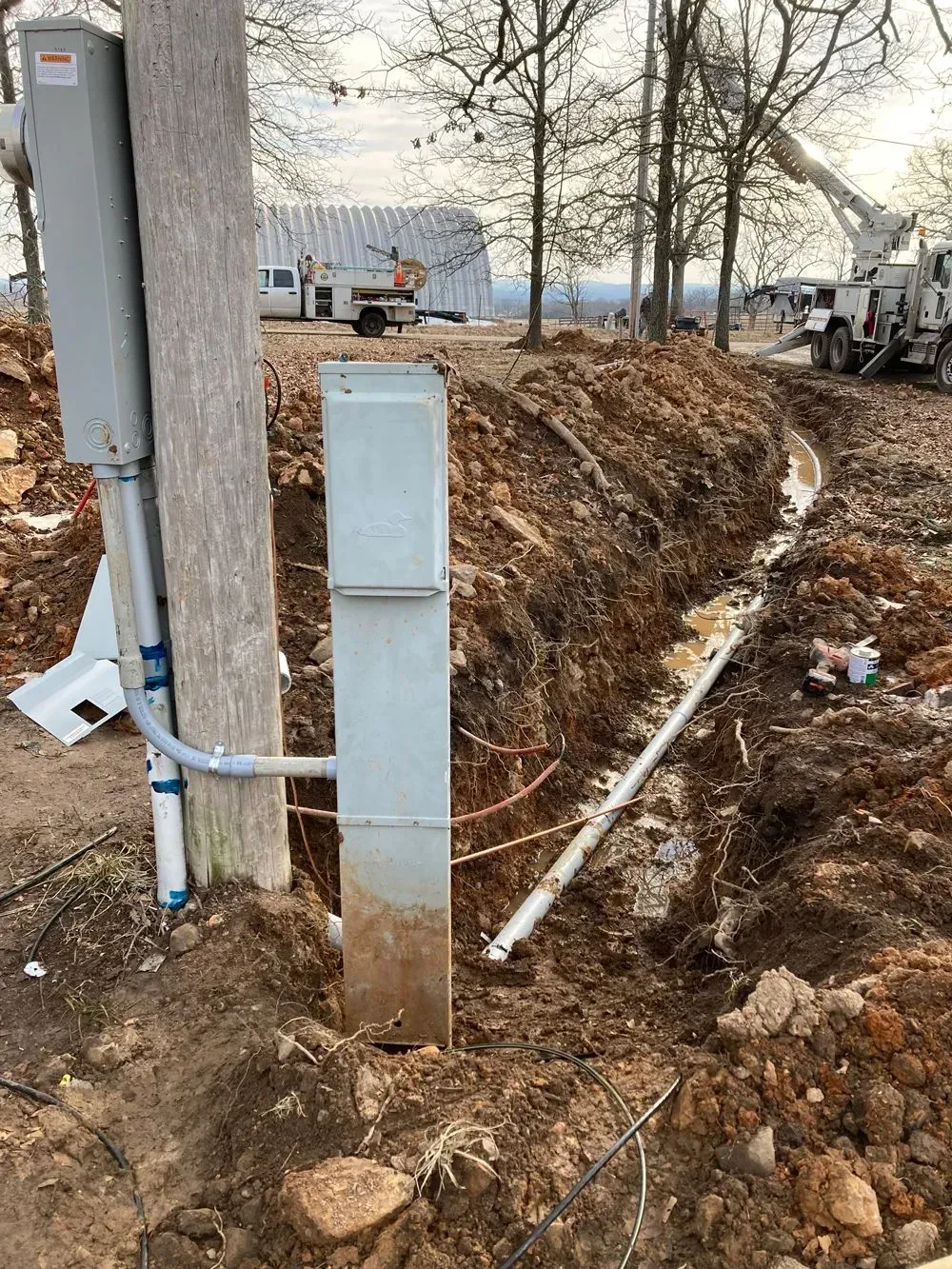 A utility box is sitting in the dirt next to a pole.