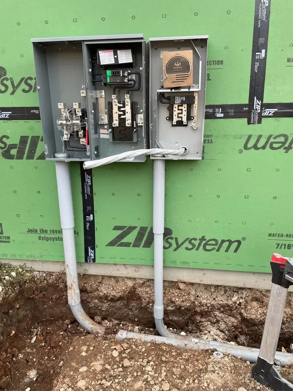 A couple of electrical boxes sitting on top of a dirt field next to a green wall.
