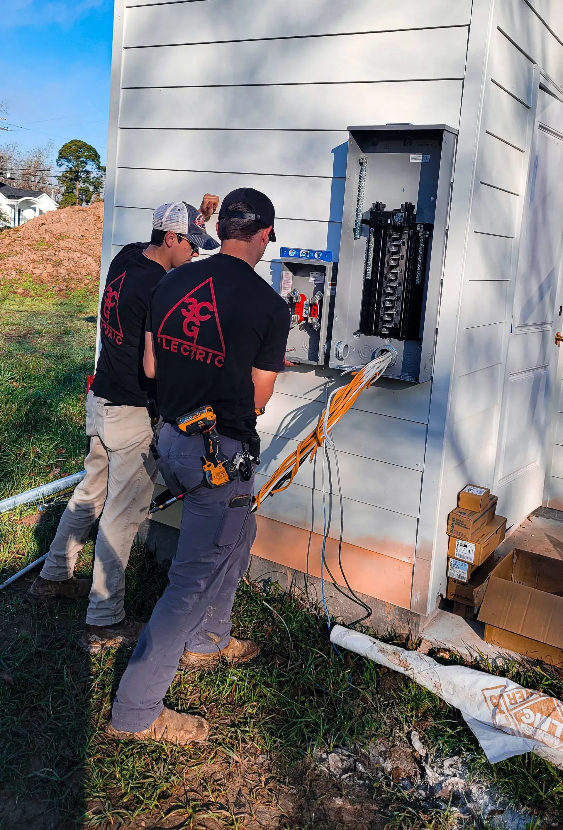 Two electricians installing electrical equipment on a building exterior.