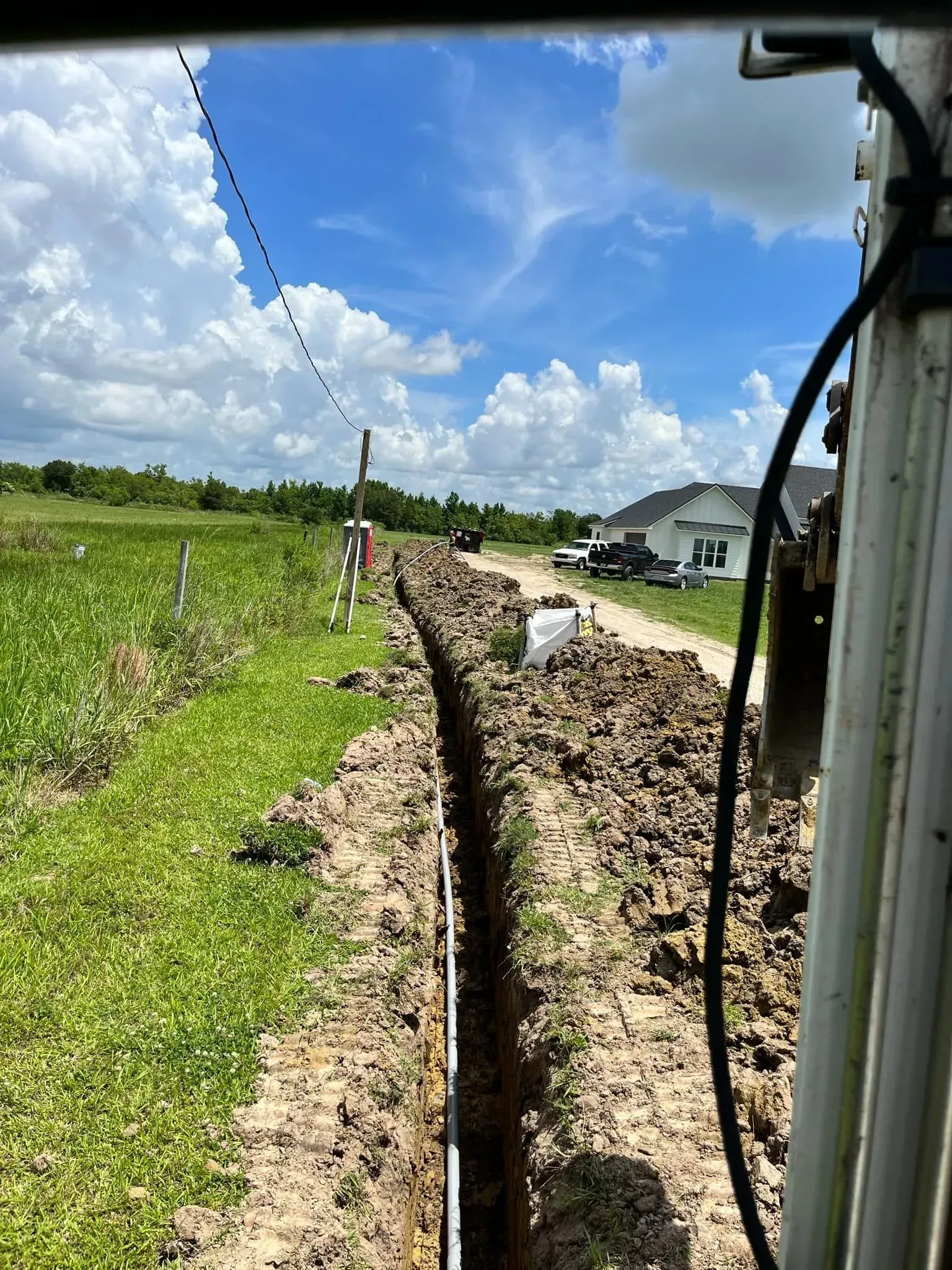 A trench dug along a grassy field with a pipeline installed, under a blue sky.
