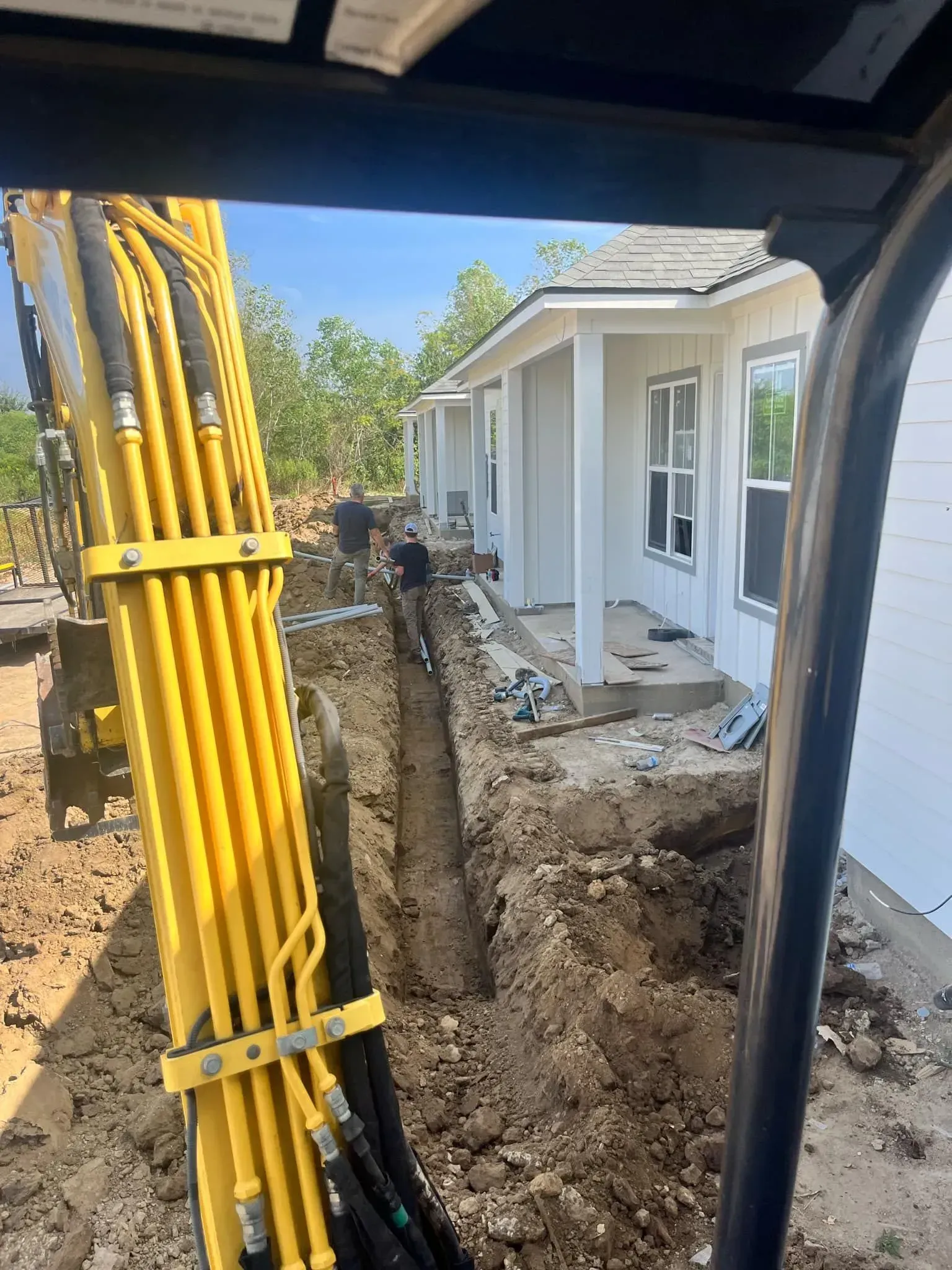 Yellow excavator digging a trench next to a white house under construction.