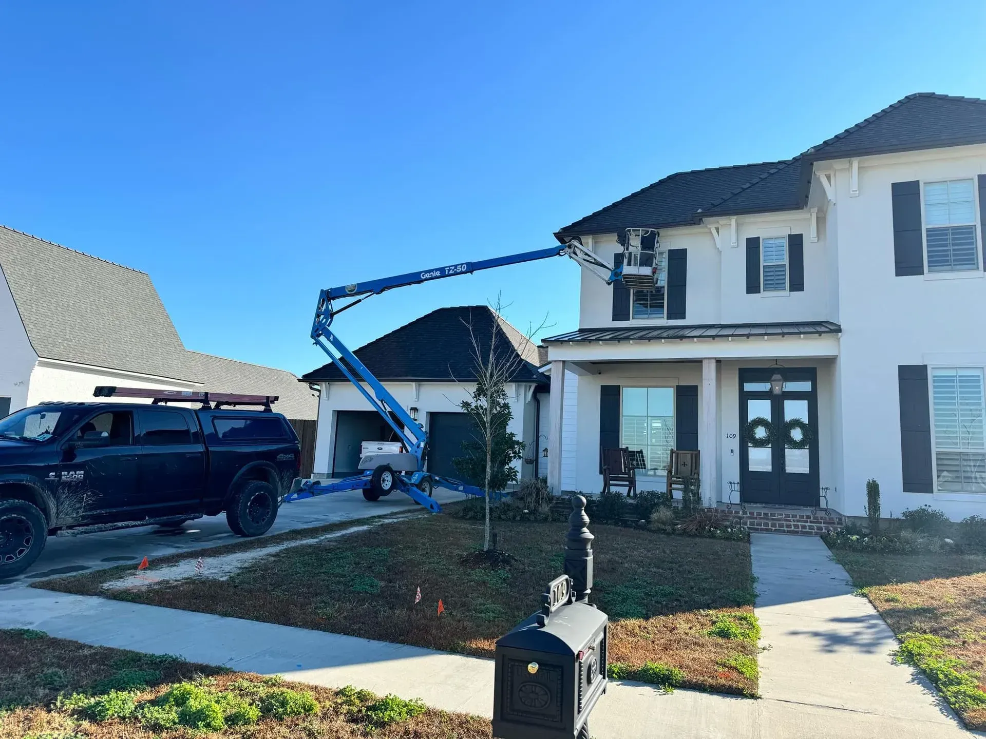 A blue lift is being used to work on the exterior of a white house on a sunny day.