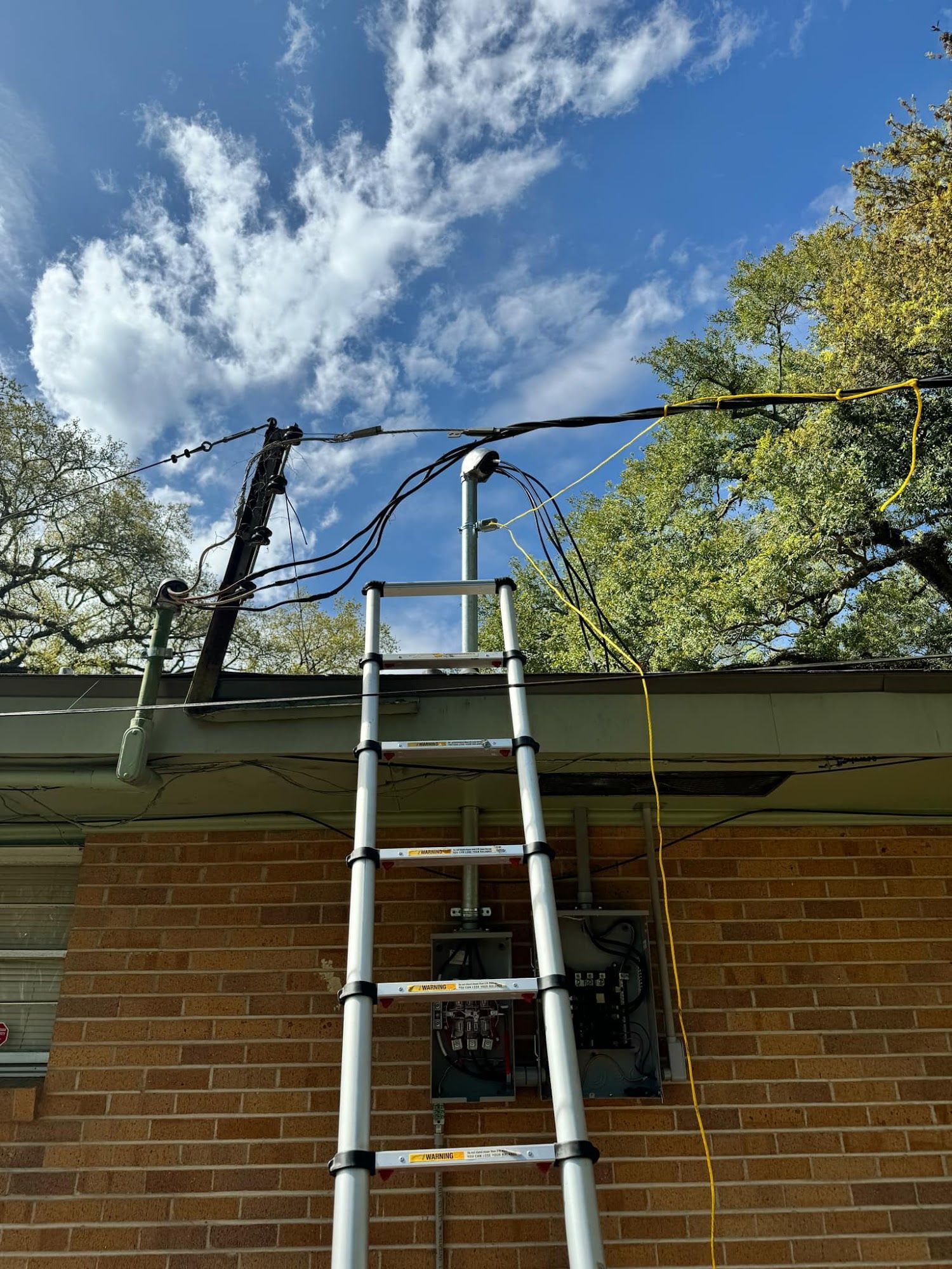 Ladder on roof, electrical equipment and wires against a partly cloudy sky.