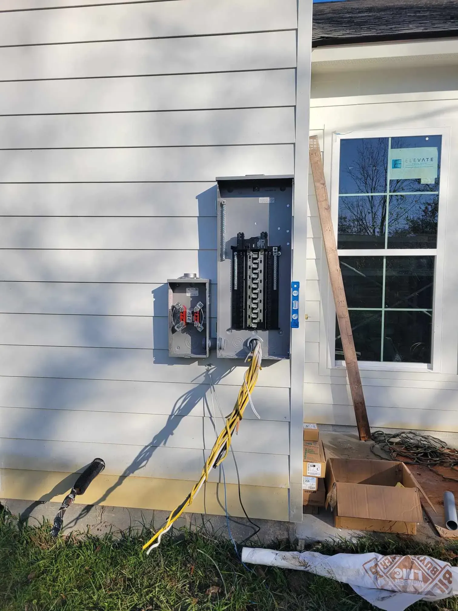 Exterior electrical panel on a white house, with exposed wires and a window under construction.