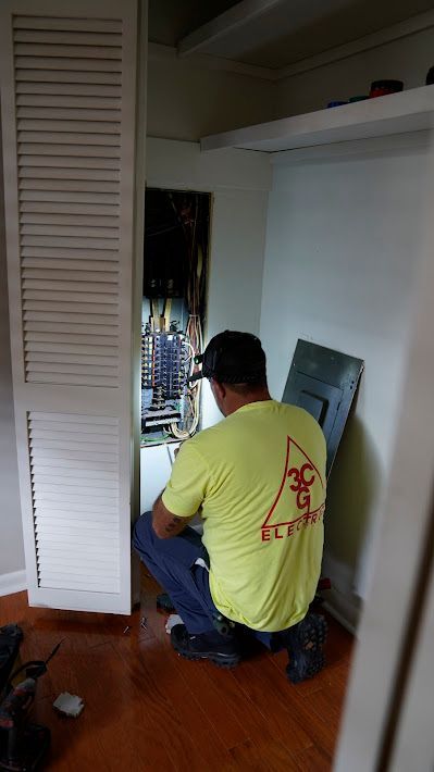 Electrician working on a circuit breaker panel in a closet. He wears a yellow shirt and a headlamp.