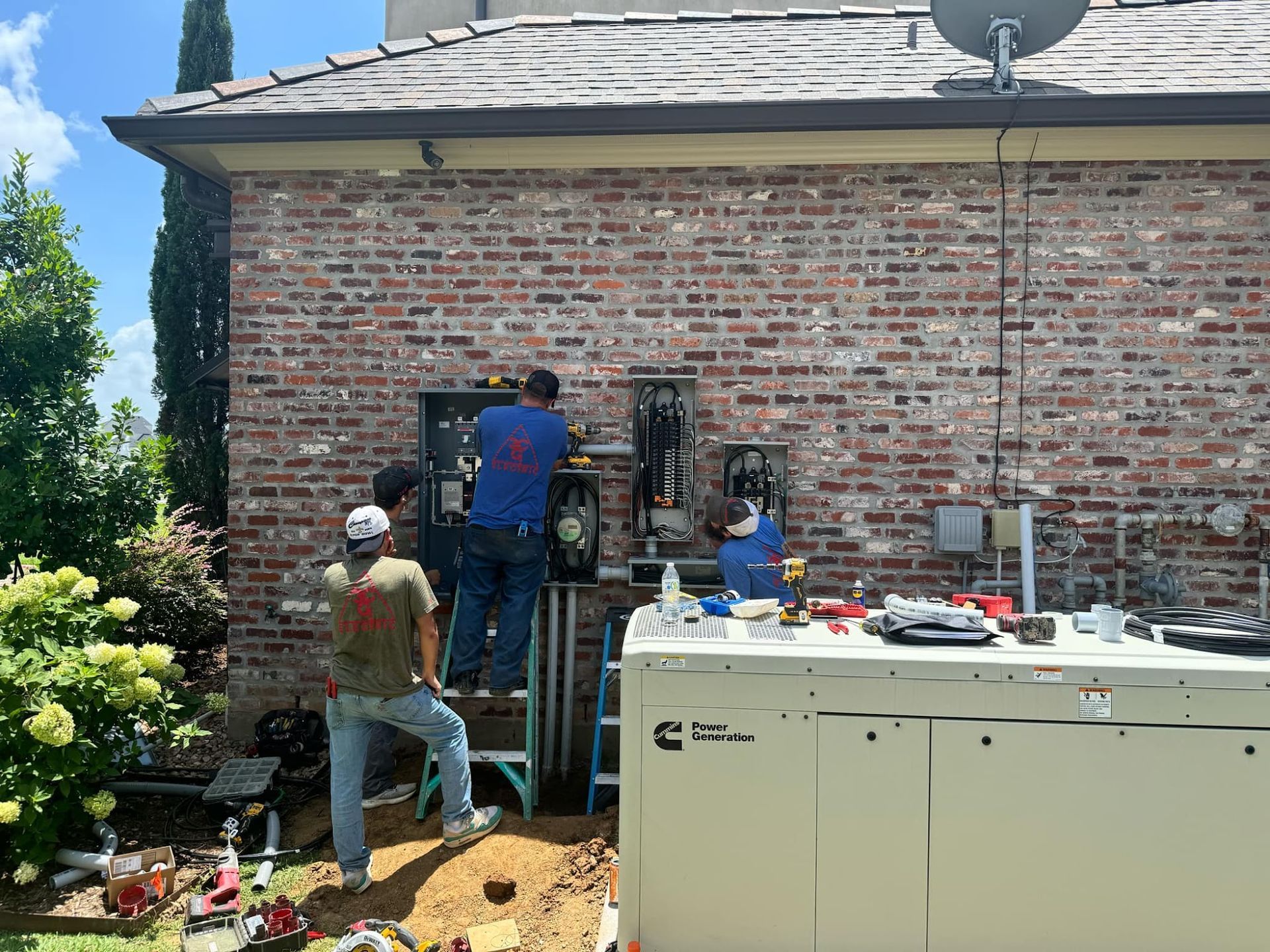 Workers installing electrical equipment on a brick building exterior, near a generator. Blue sky.