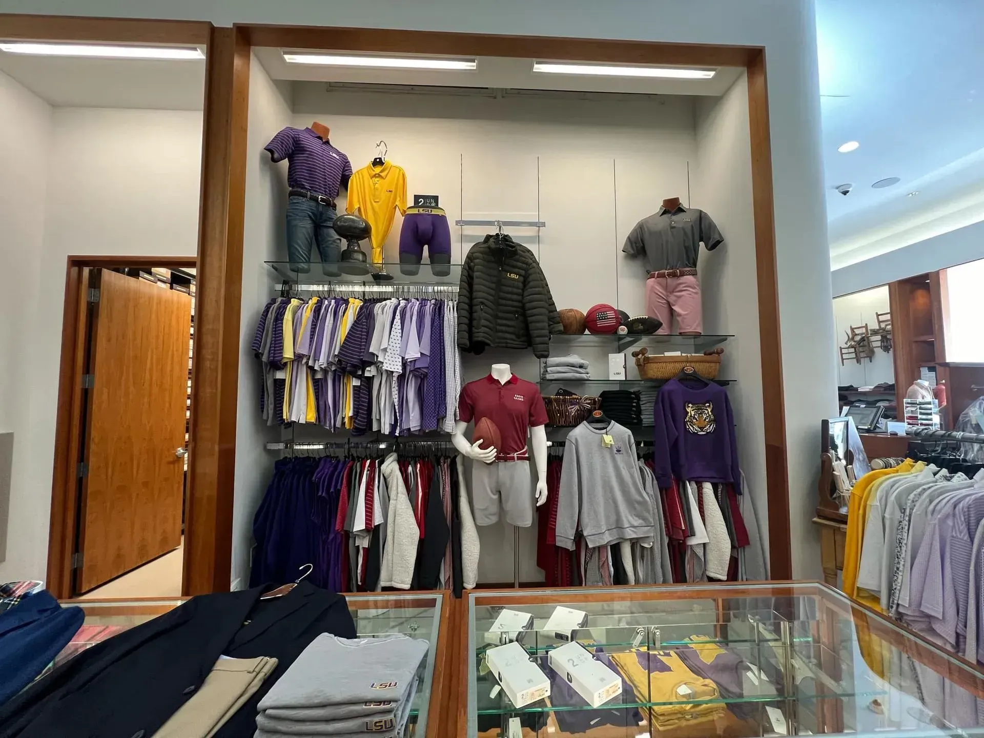 Clothing display in a store, purple and gold clothing, mannequins, shelves, door on left.