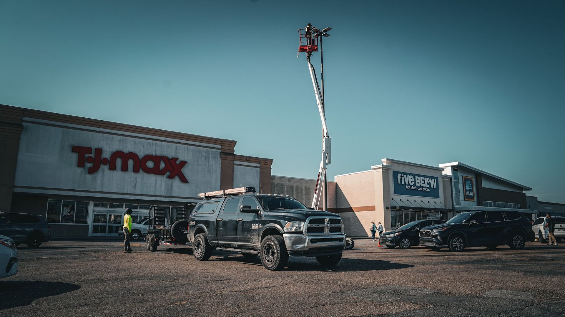 Dark truck parked in front of TJ Maxx and Five Below stores, with a tall crane in the background.