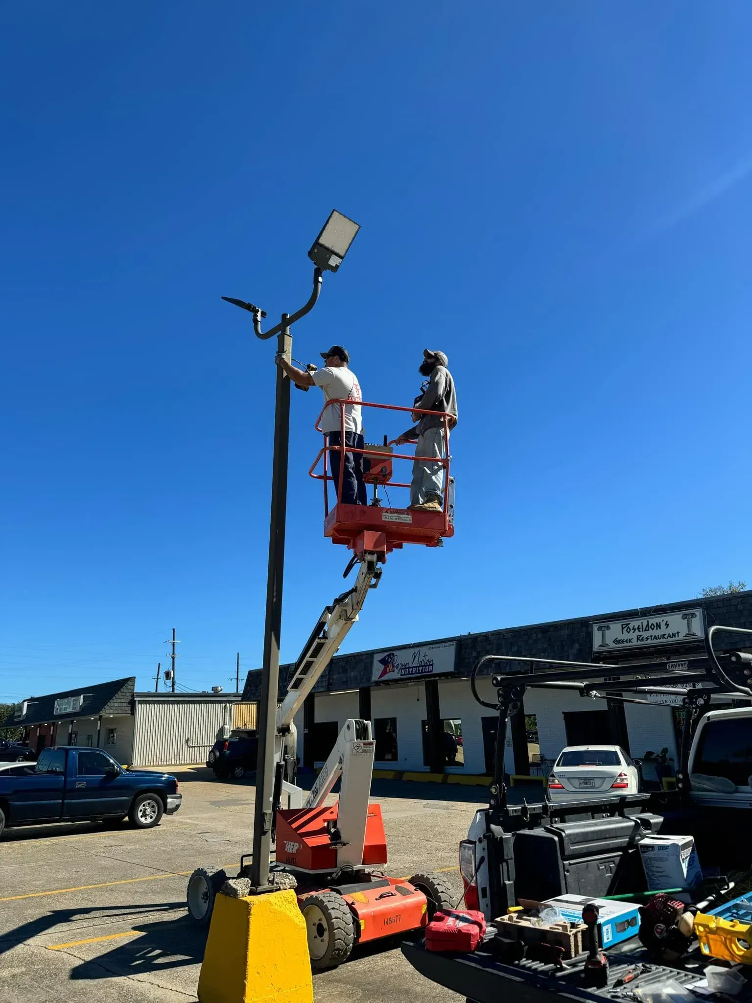 Two workers on a cherry picker installing a street light against a clear blue sky.
