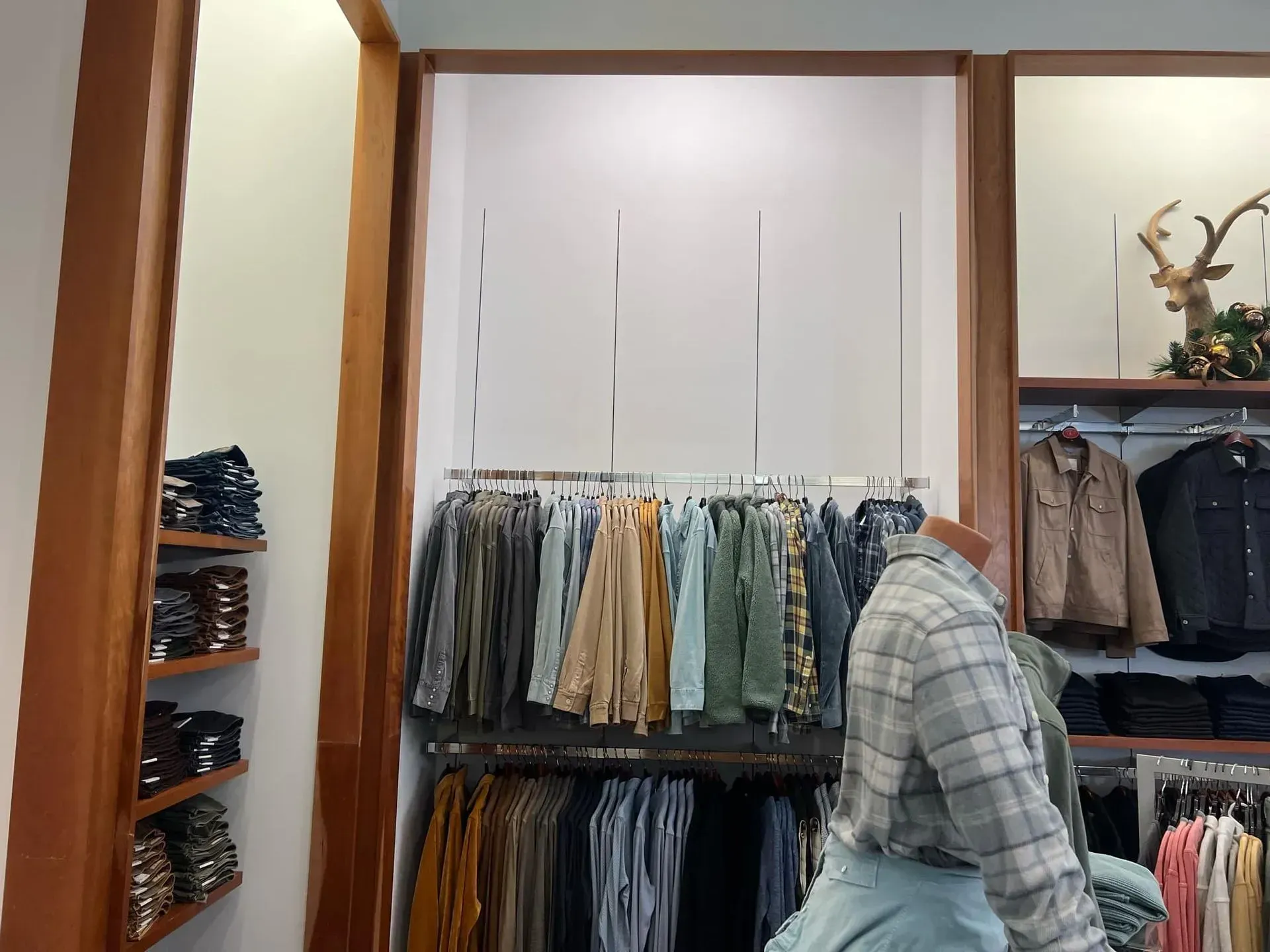 Clothing store display with shirts and jeans on racks and shelves. Mannequin wearing a plaid shirt.