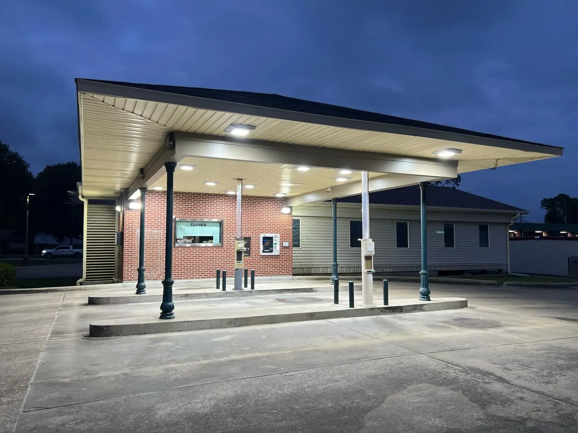 Drive-thru ATM under a covered area, red brick wall, illuminated at dusk.