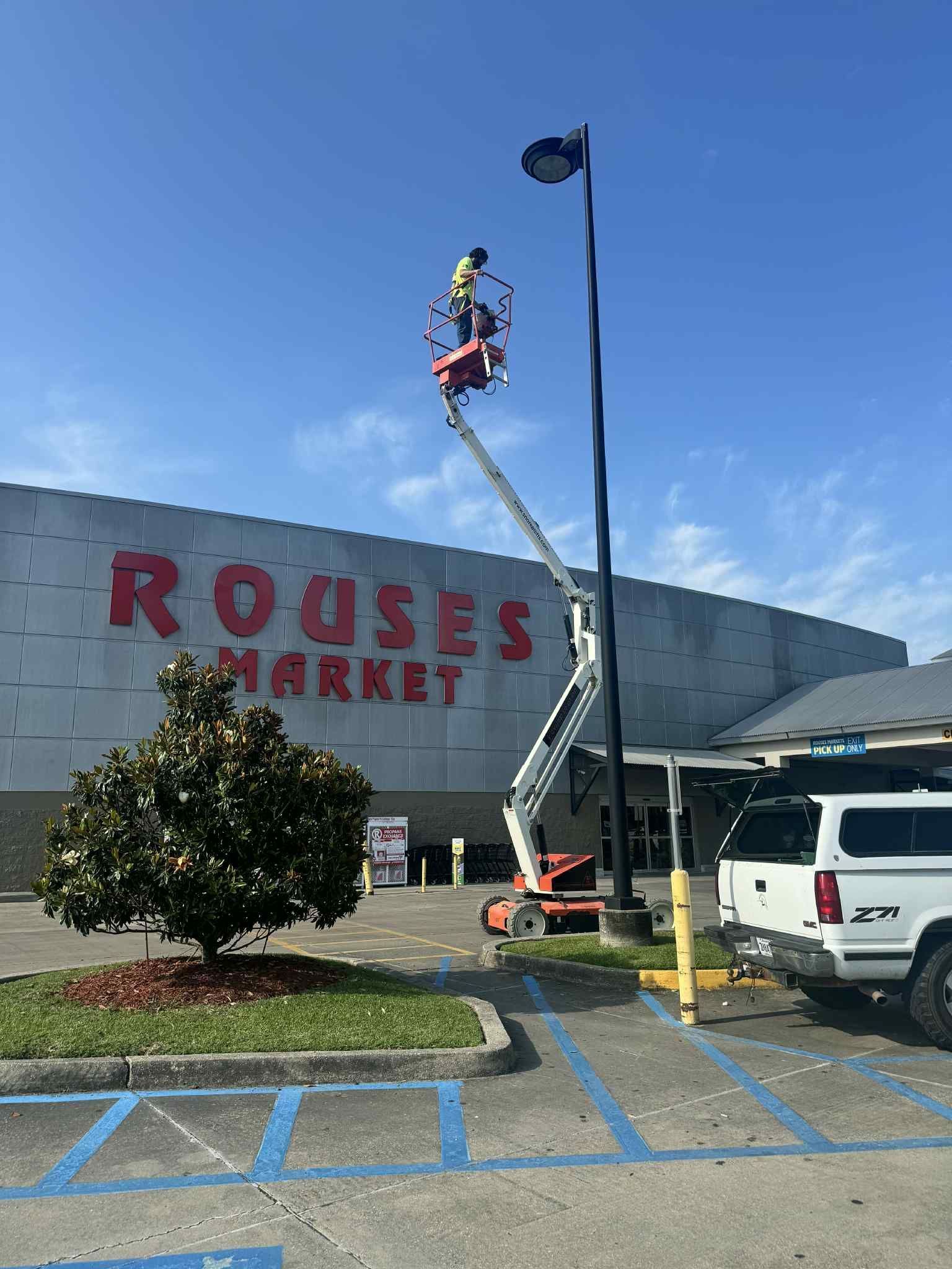Person in a lift working on a light fixture outside a Rouses Market.
