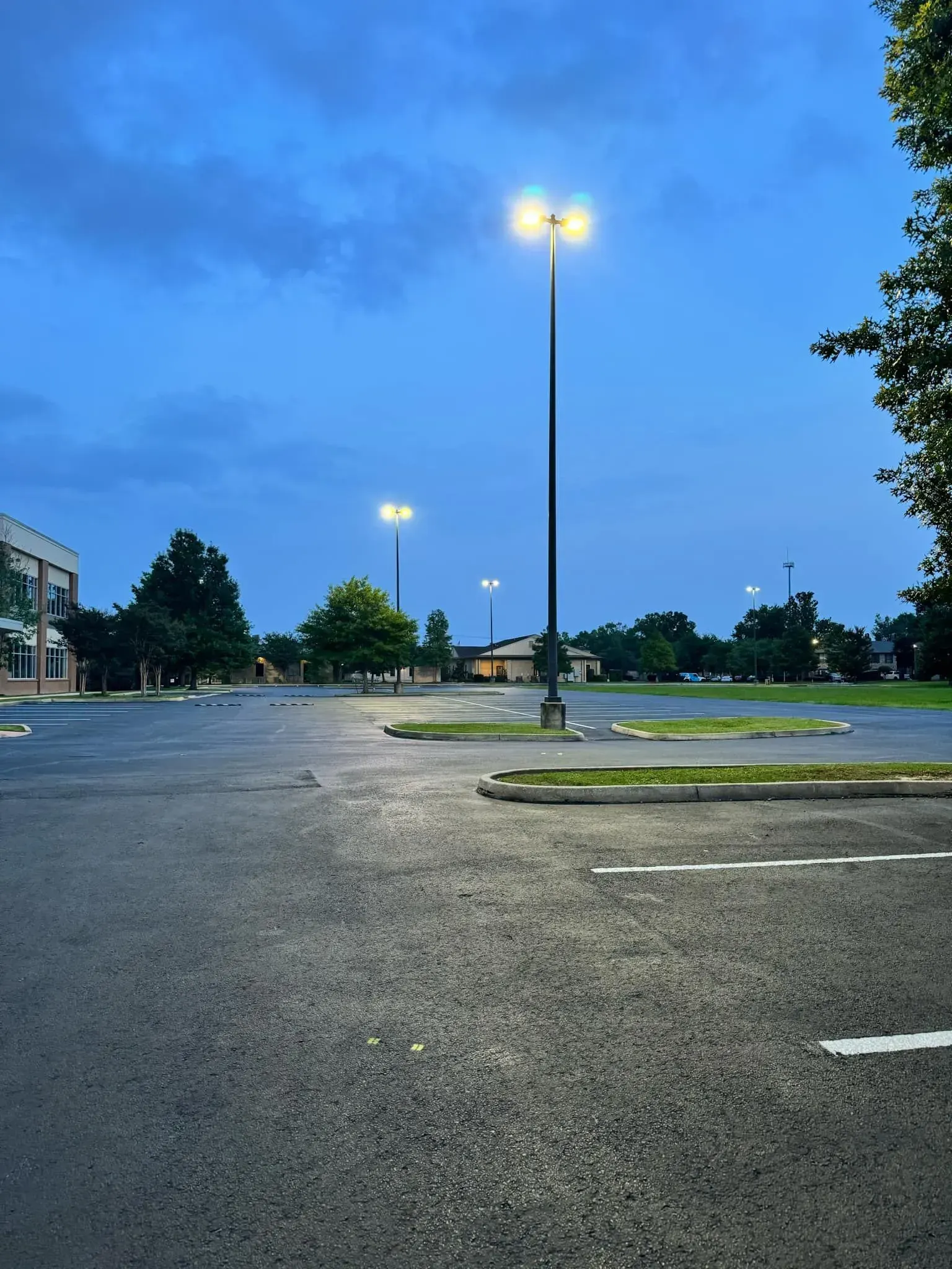 Empty parking lot under a cloudy blue sky, lit by tall streetlights.