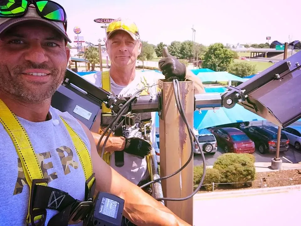 Two men installing solar panels on a sunny day, one giving a thumbs up.