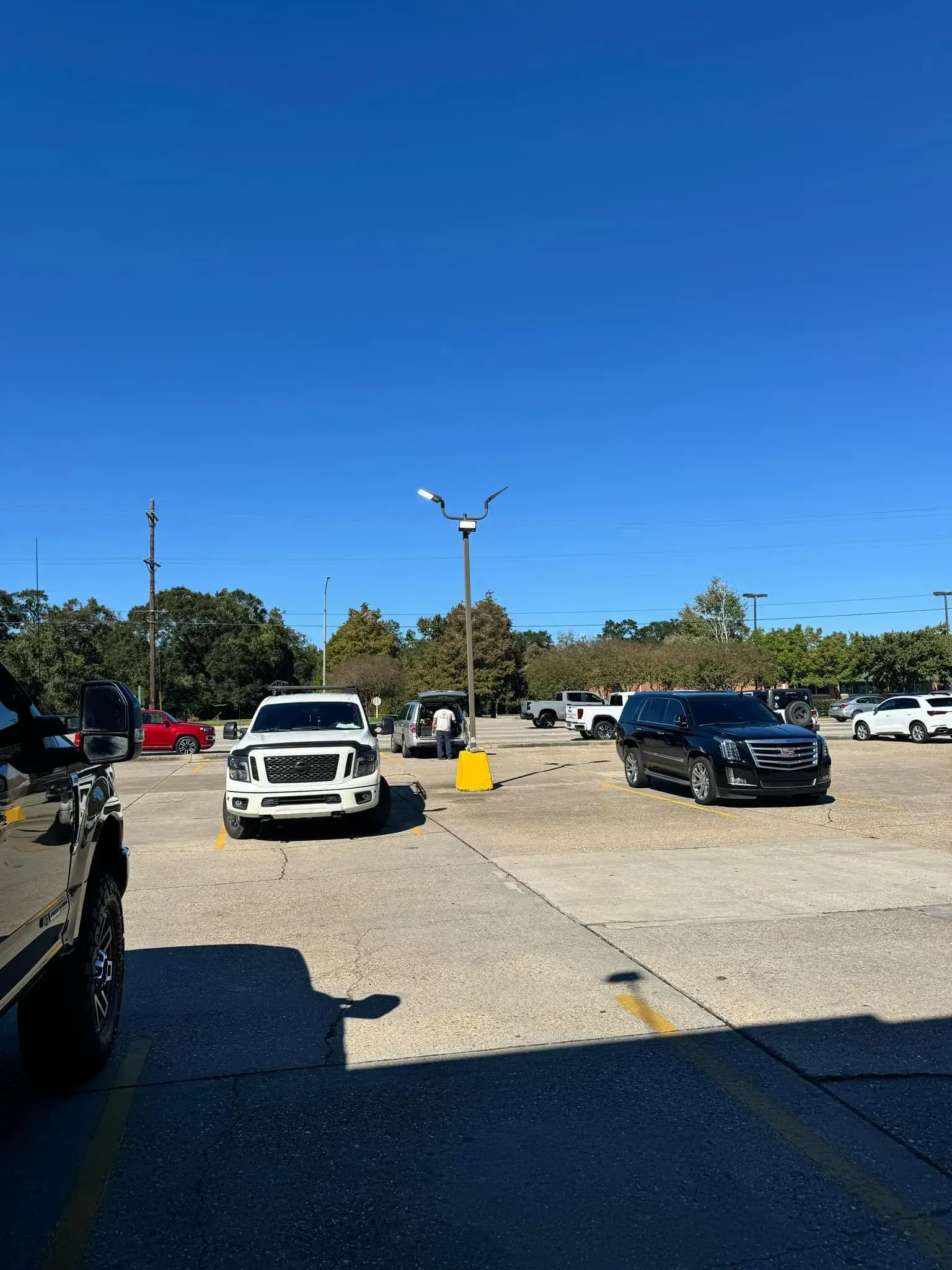 Vehicles parked in a lot under a clear blue sky. A white truck and black SUV are prominent.