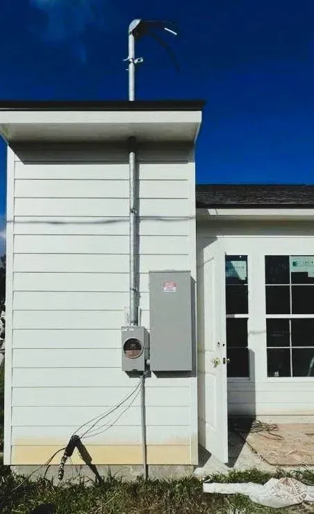 A utility pole and metal electrical box on a white building against a blue sky.