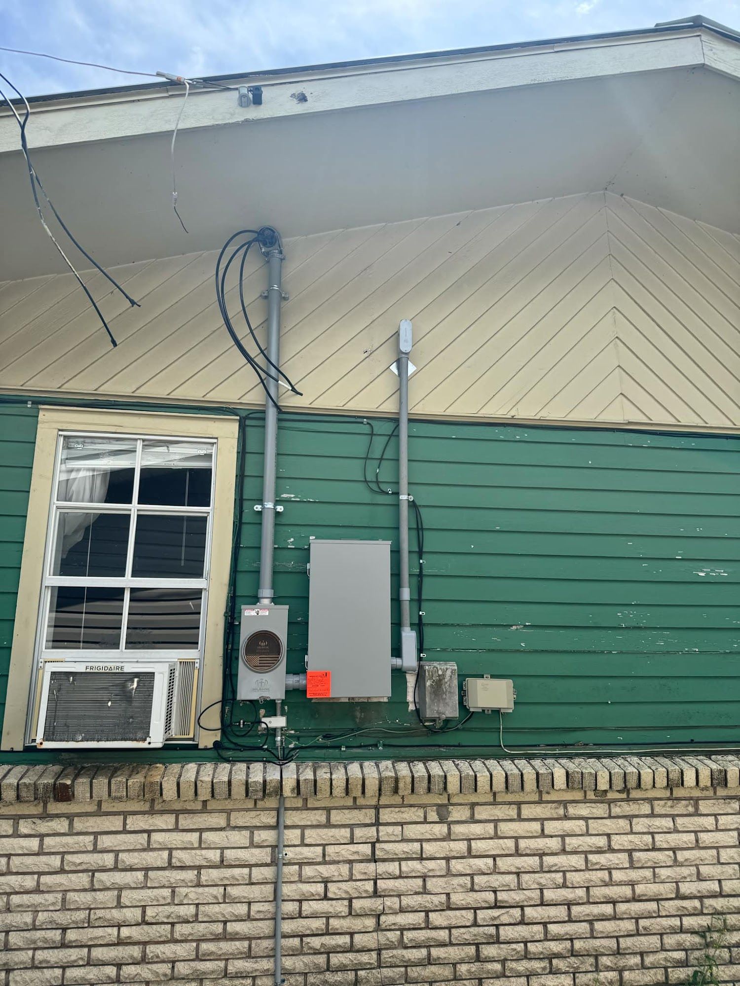 Exterior of a green building with electrical equipment, including a meter box and conduit.