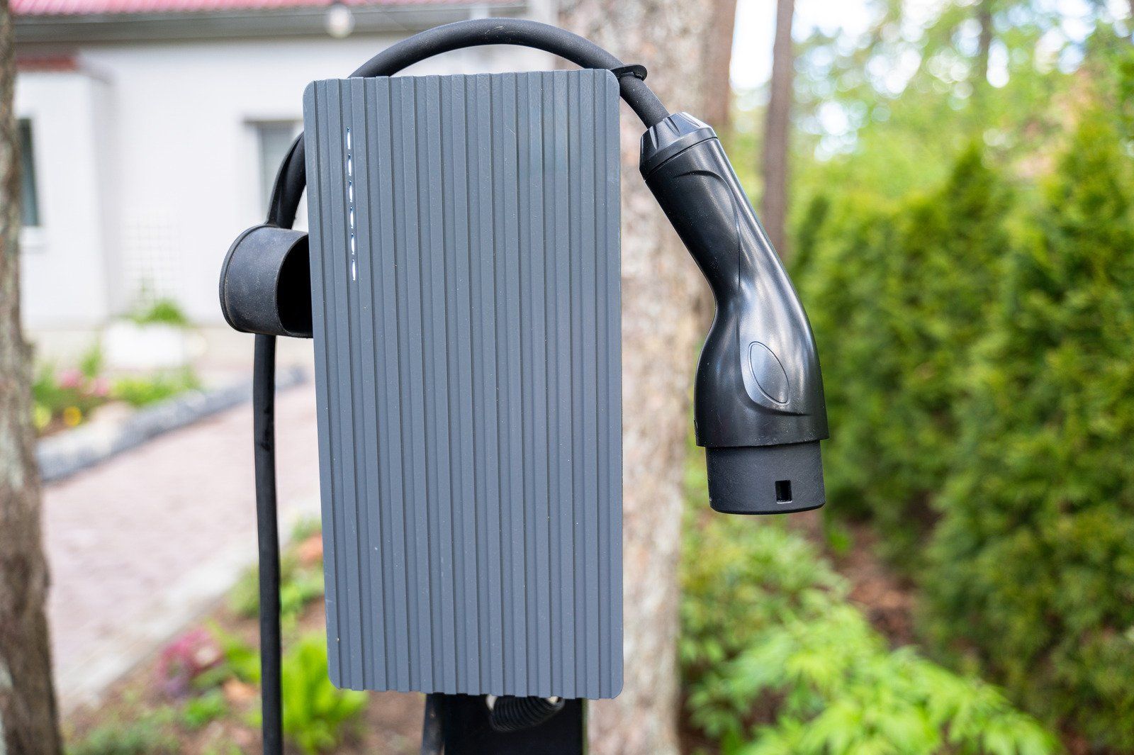 Gray electric vehicle charger mounted on a post in a yard.