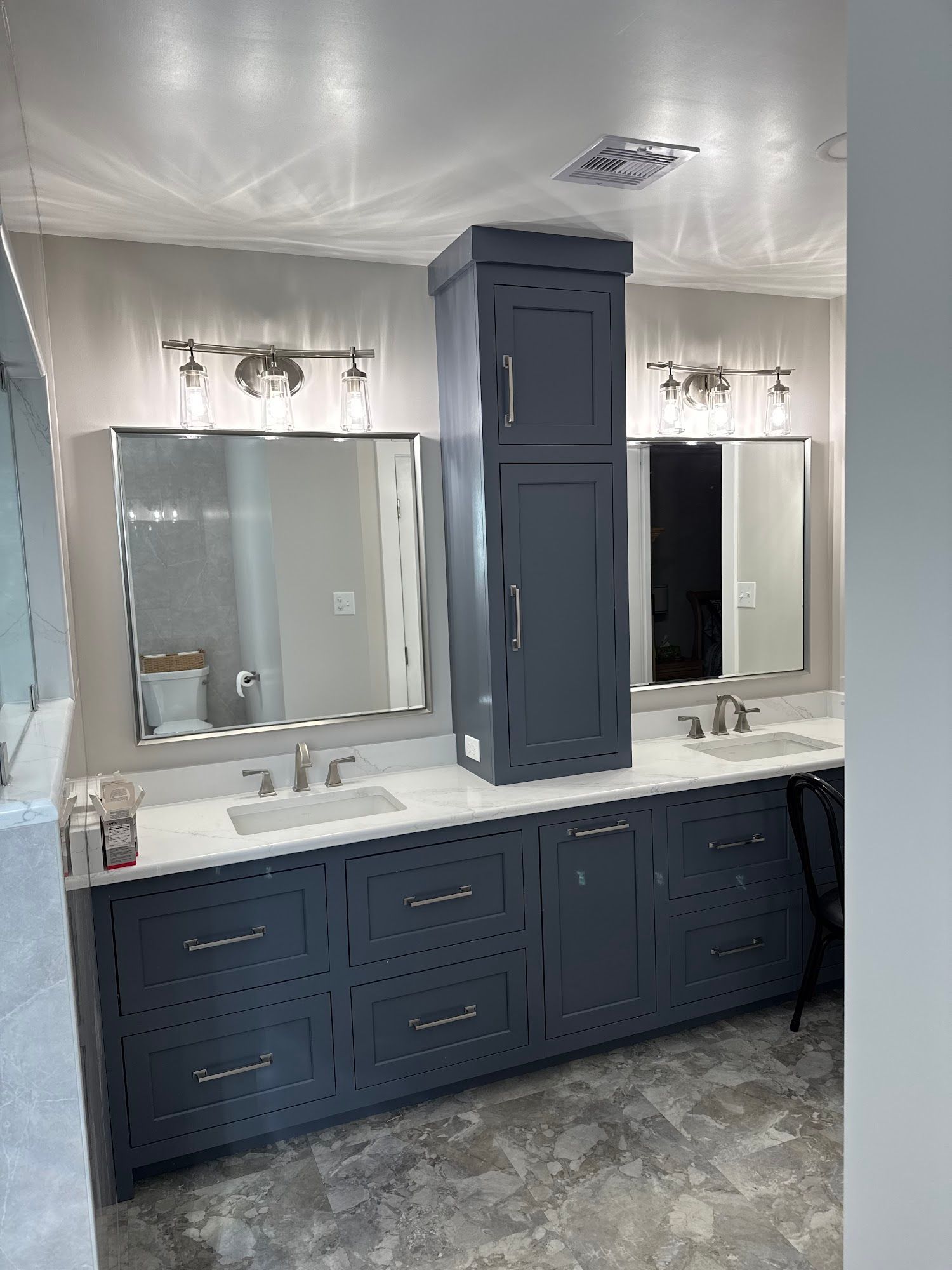 Bathroom with blue cabinets, white countertops, two sinks, mirrors, and a tall storage cabinet.
