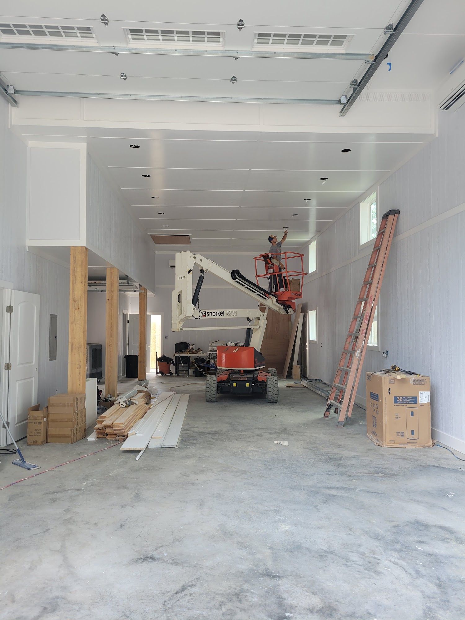 Construction site interior: workers on lift, framing, drywall, concrete floor, wooden beams, ladder, boxes.