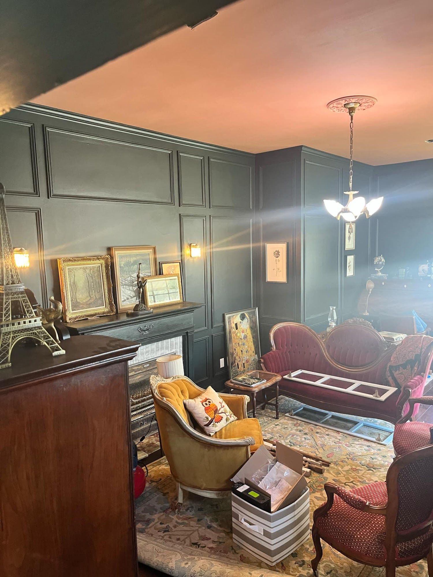 Dark-walled living room with ornate furniture, fireplace, and Eiffel Tower model.