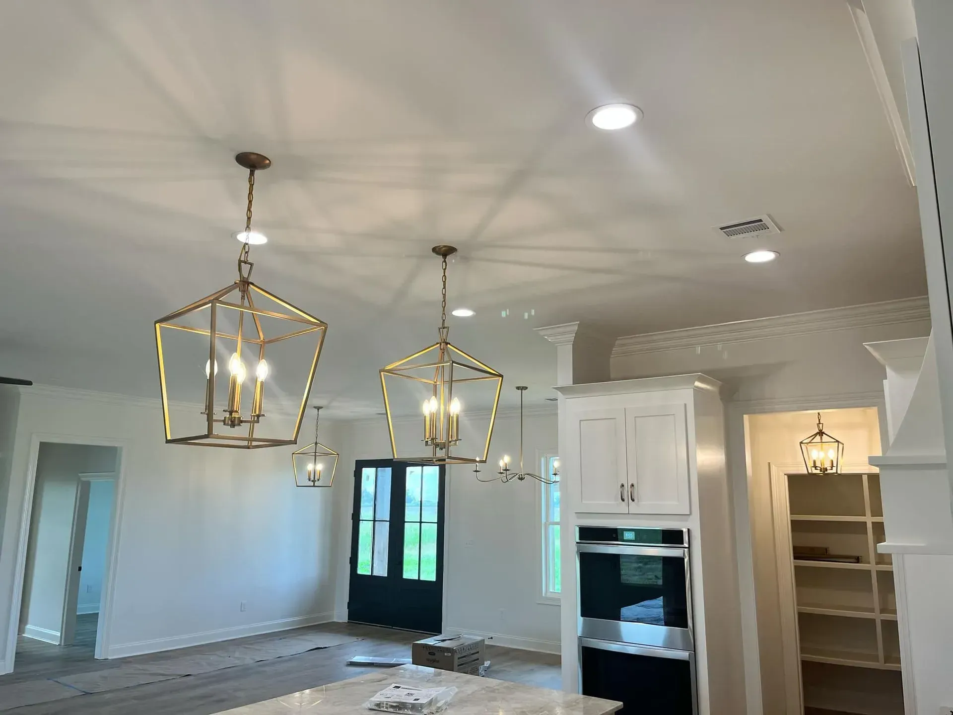 Two gold pendant lights hanging in a white kitchen with recessed lighting, green door, and white cabinets.
