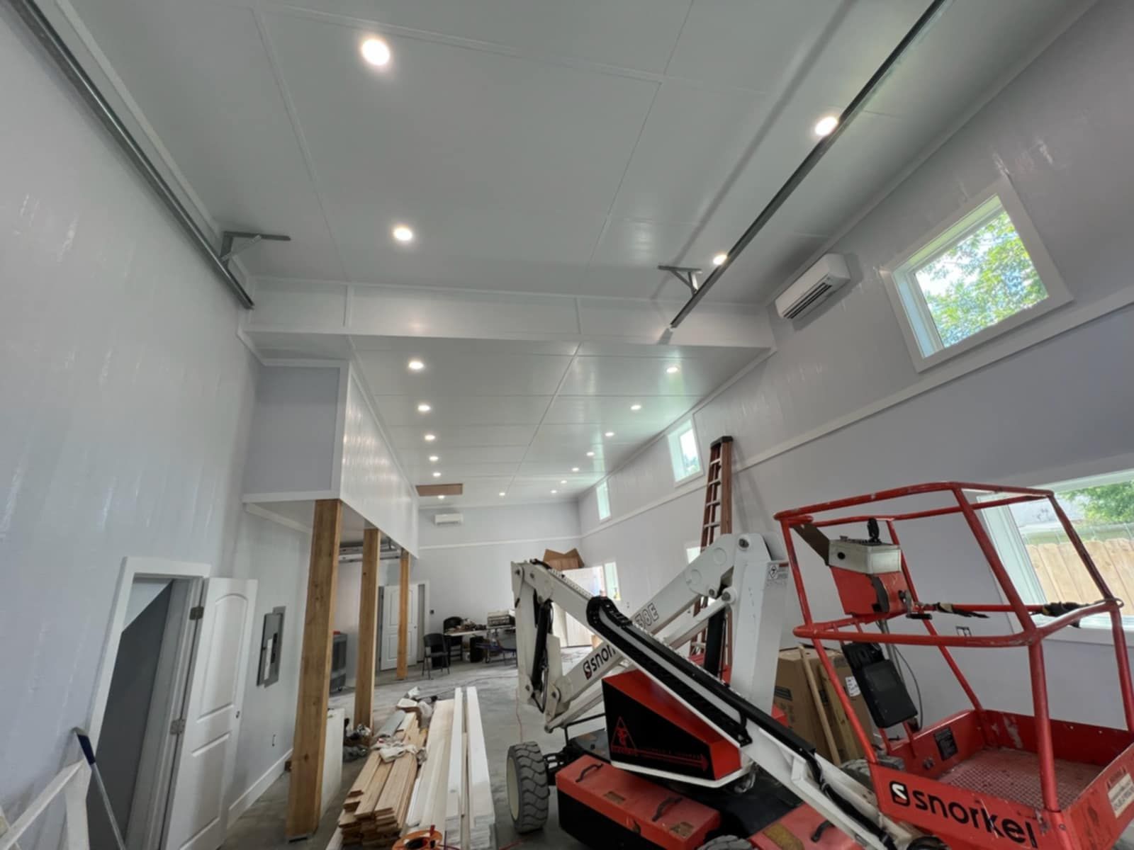 Interior of a building under construction, white walls and ceiling, a lift, tools, windows, and exposed beams.