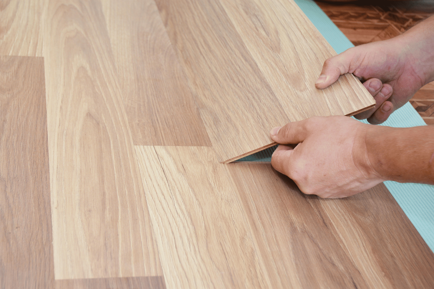 Hands fitting a wooden floor plank into place.