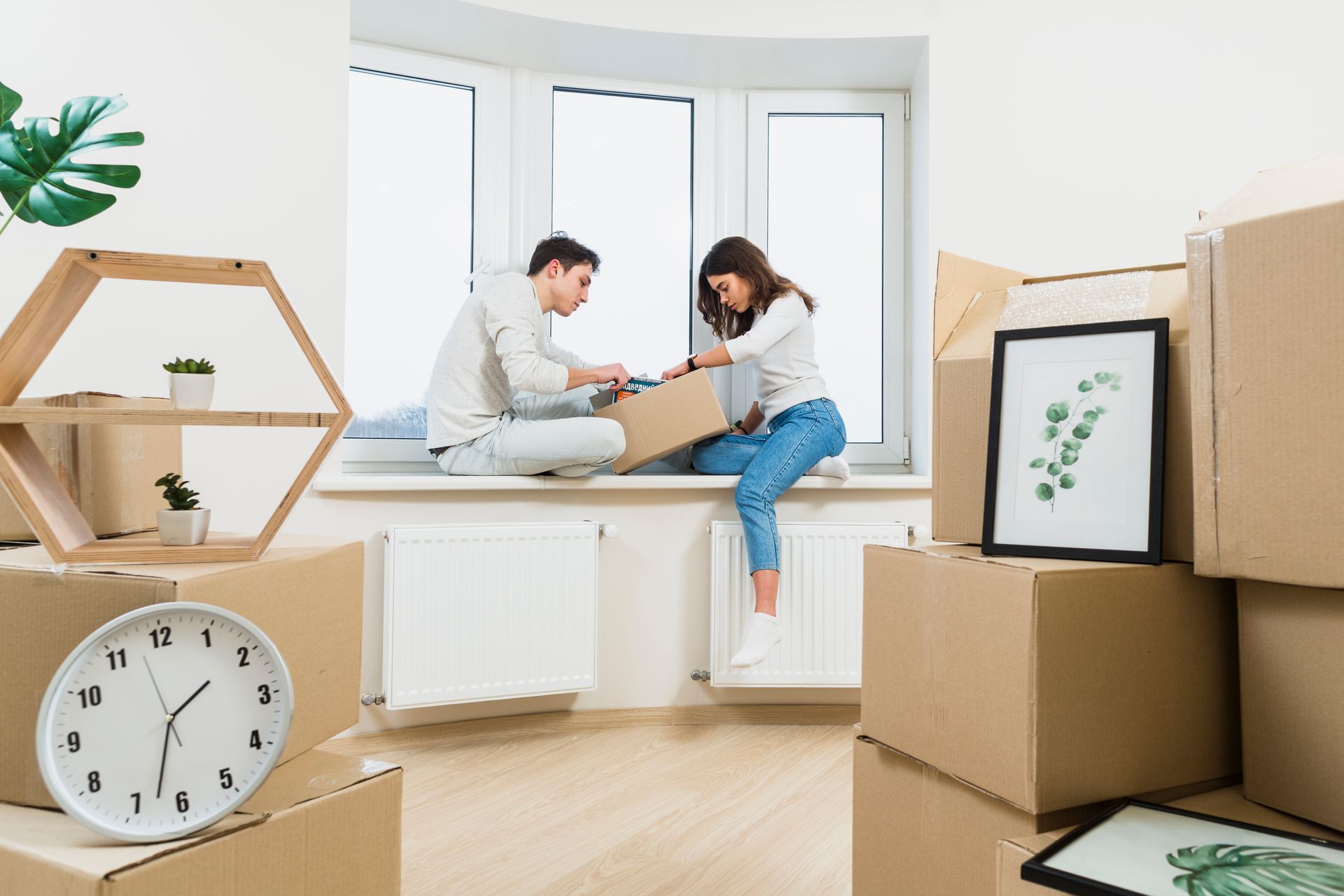 A man and a woman are sitting on a window sill surrounded by cardboard boxes.