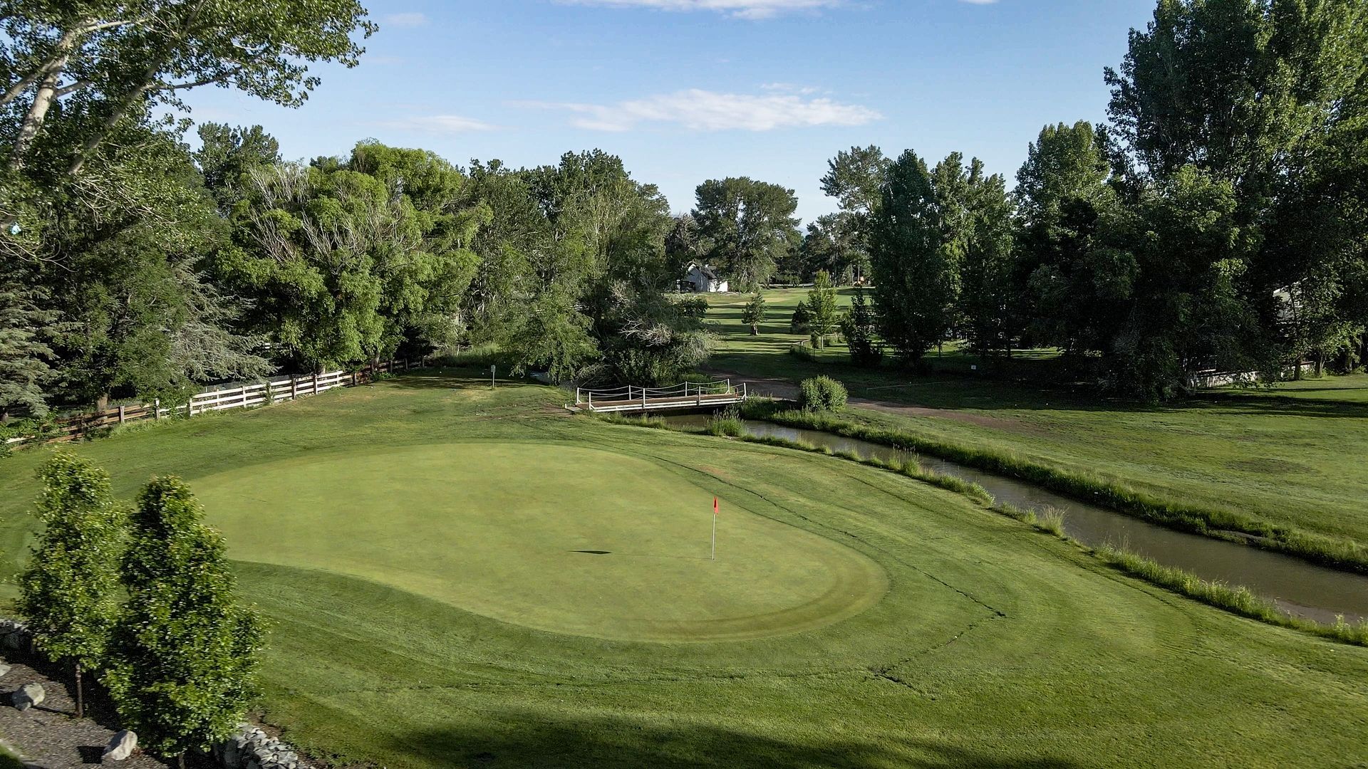 An aerial view of a golf course with a green and trees in the background.