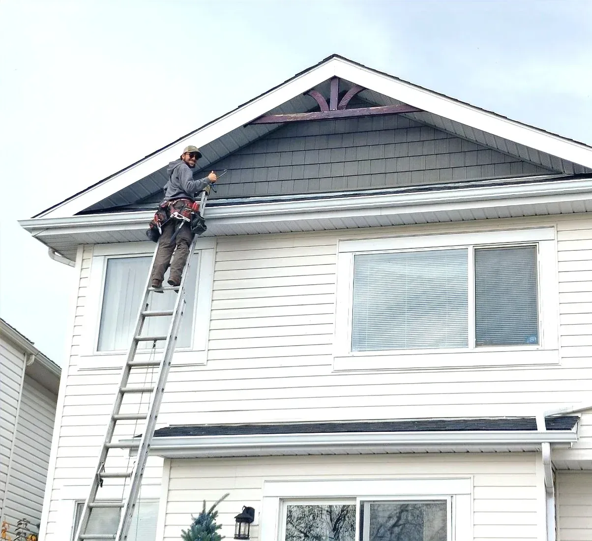 A man is standing on a ladder on the side of a house.