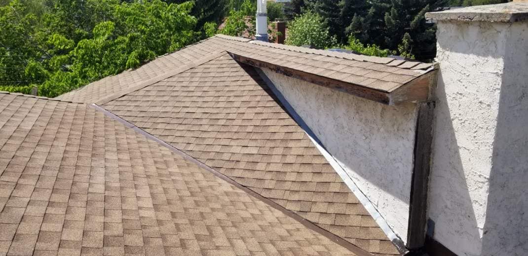 A roof with a chimney on the side of it and trees in the background.