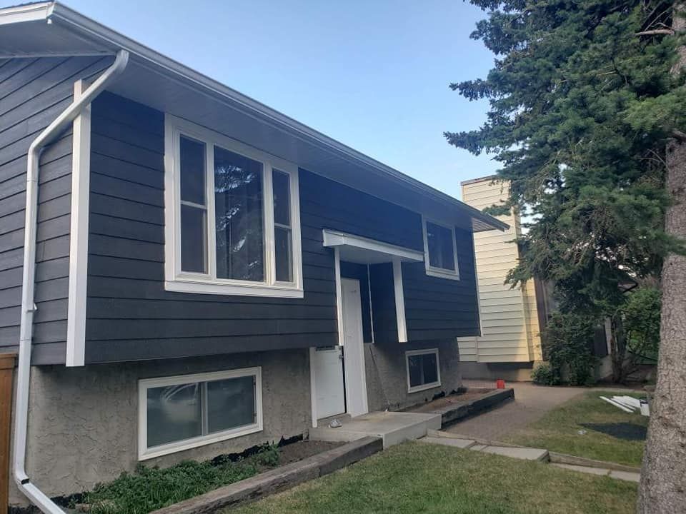 A house with a black siding and white windows is sitting next to a tree.